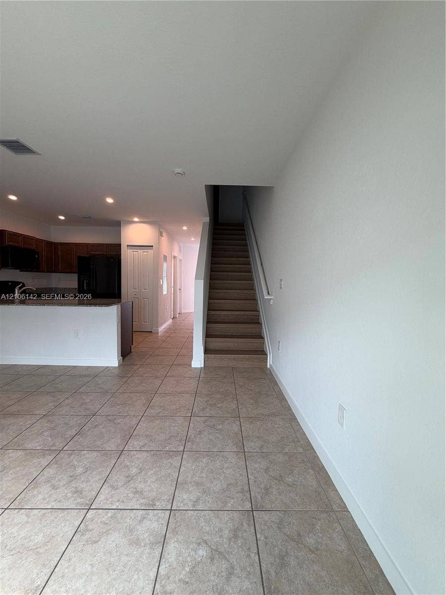 Open-concept interior featuring large-format tile flooring, recessed lighting, and a staircase with a handrail