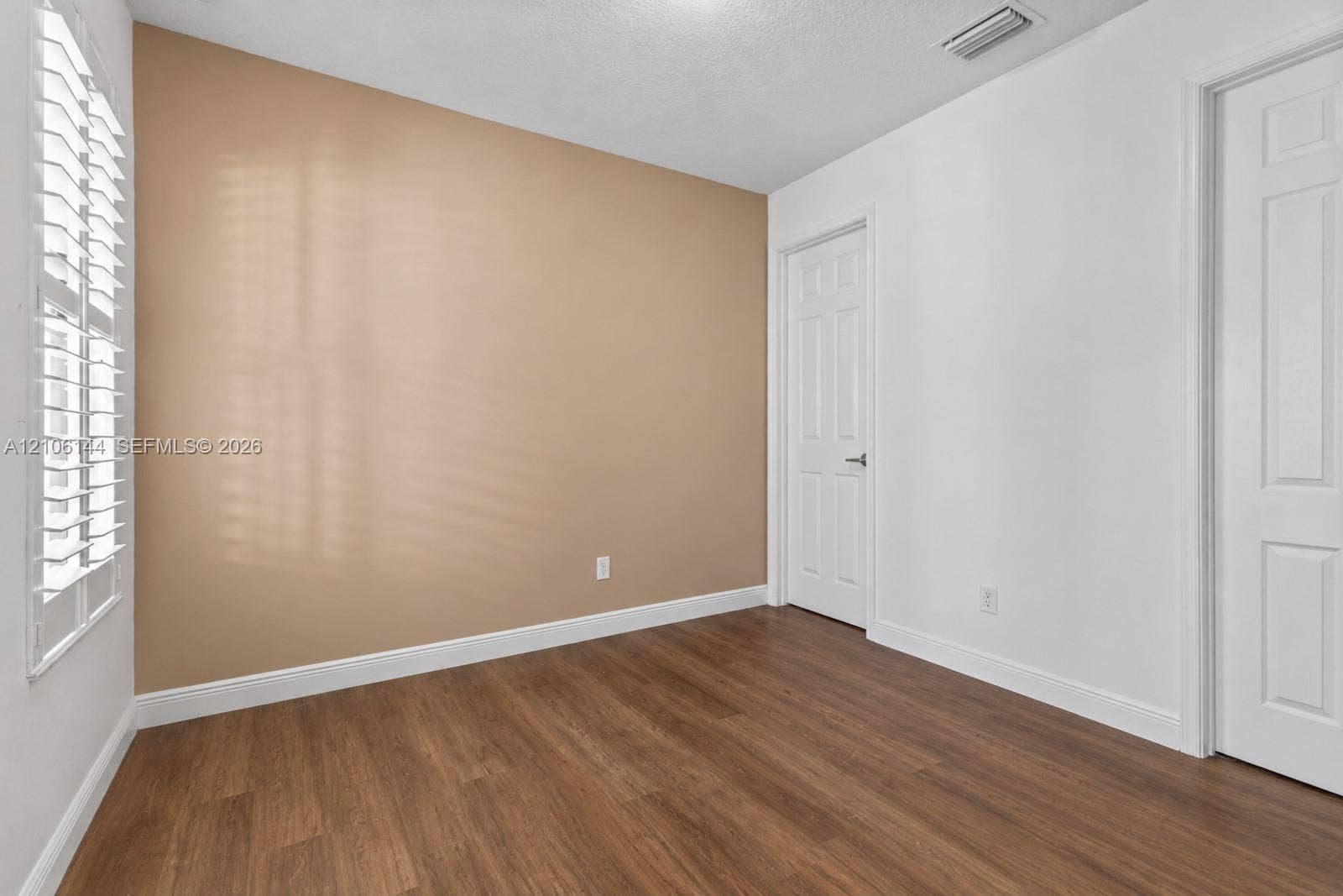 Room featuring wood-finish flooring, plantation shutters, and two multi-panel doors