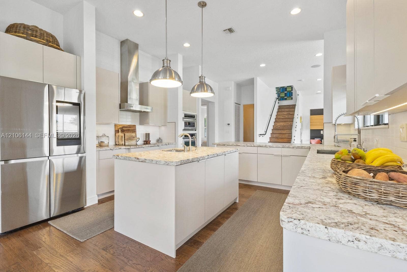 Kitchen featuring a central island with stone-style countertops, stainless steel appliances, flat-panel cabinetry, and pendant lighting over wood-finish flooring