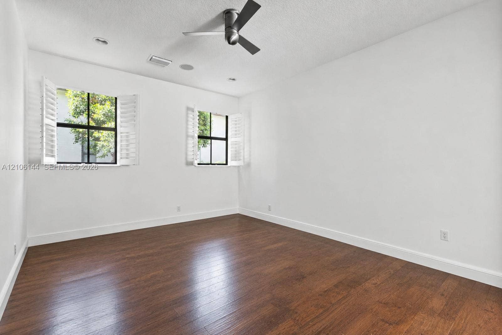 Wood-finish flooring, dual windows with plantation shutters, and a ceiling fan