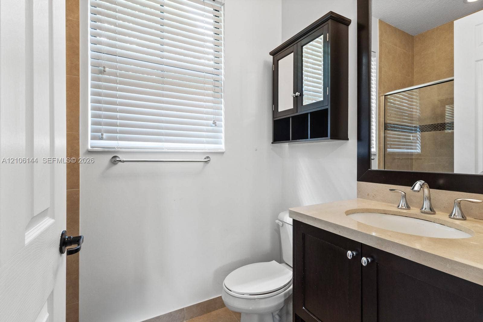 Dark wood-finish vanity with a stone countertop, integrated undermount sink, matching wall-mounted storage cabinet, and tiled flooring