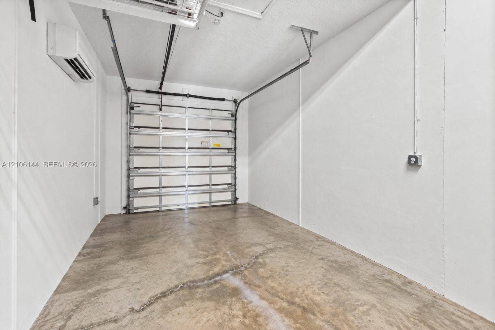 Enclosed garage featuring finished white walls, a metal sectional door, and a wall-mounted ductless climate control unit