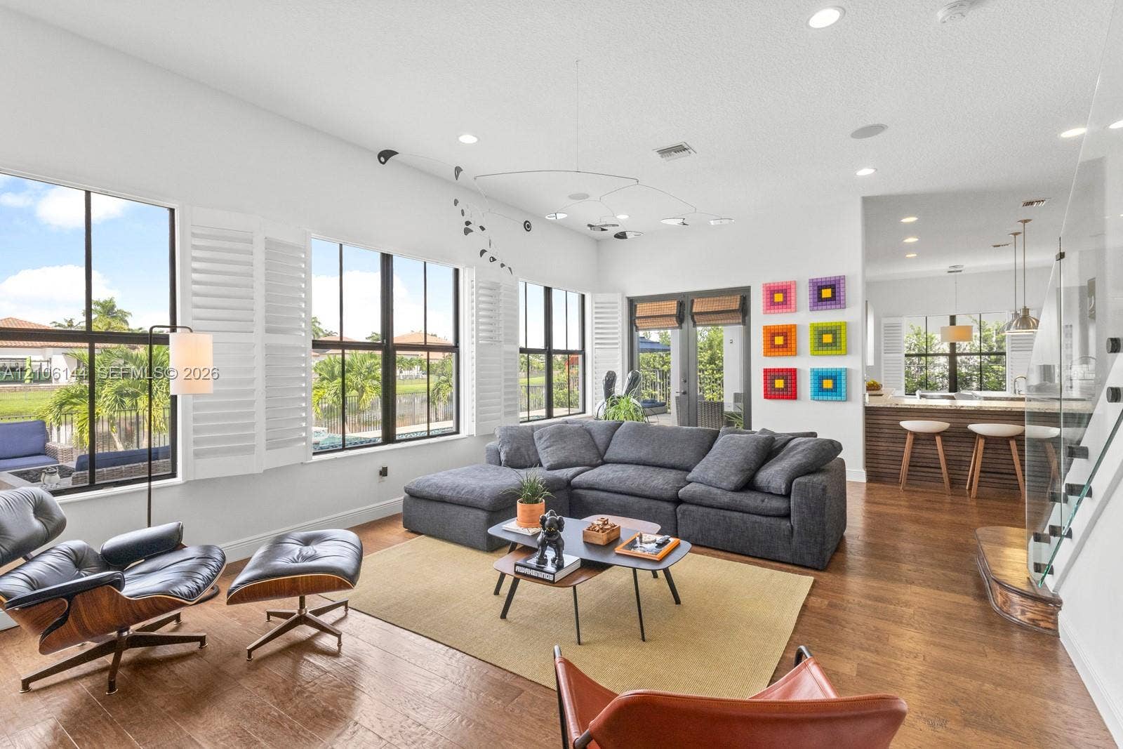Open-concept living space featuring wood-finish flooring, floor-to-ceiling windows with plantation shutters, recessed lighting, and a glass-paneled staircase