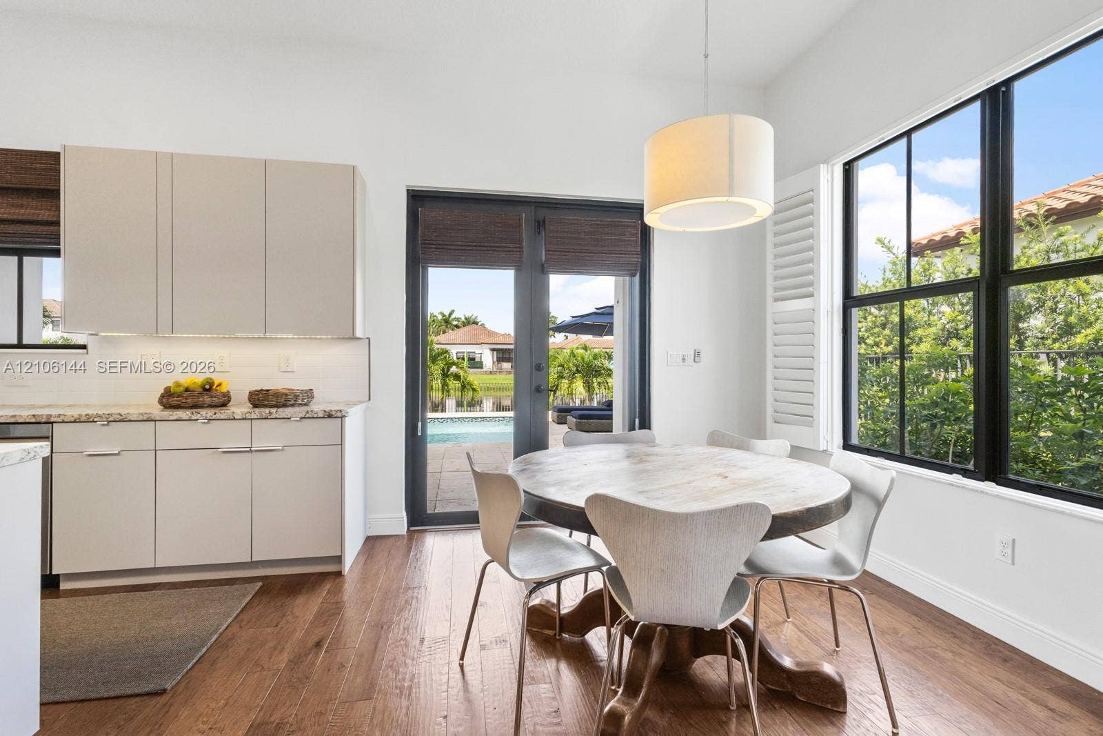 Kitchen area featuring light-toned flat-panel cabinetry, stone countertops, wood-finish flooring, full-height windows with black frames, and a glass-paneled entry door