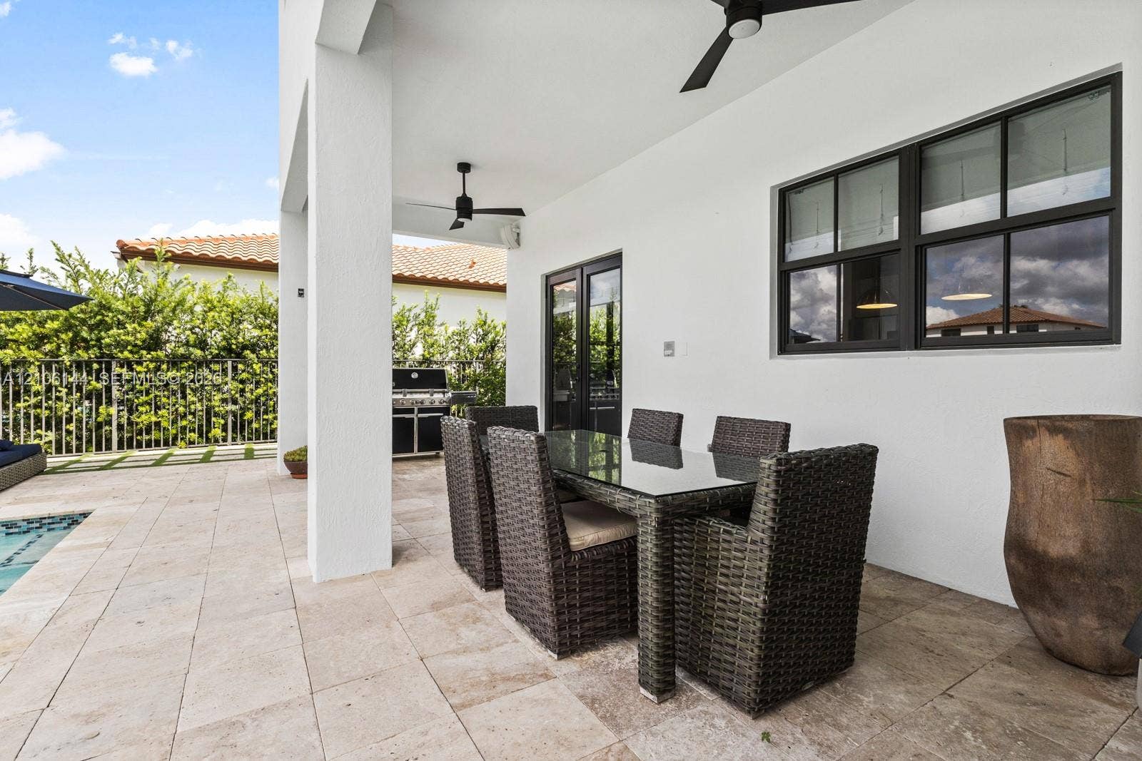 Covered patio featuring stone tile flooring, black-framed windows, and ceiling-mounted fans