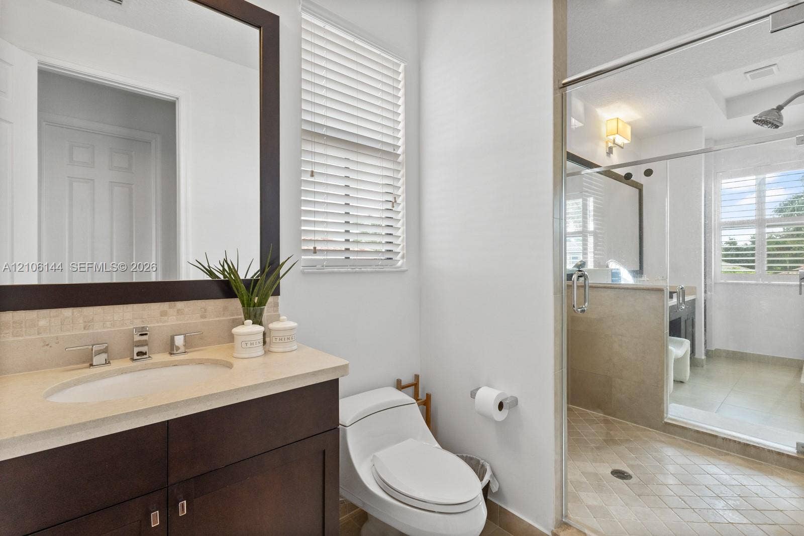 Dark-finish wood vanity with a stone countertop and integrated sink, complemented by a mosaic tile backsplash and a glass-enclosed shower with diamond-pattern tile flooring