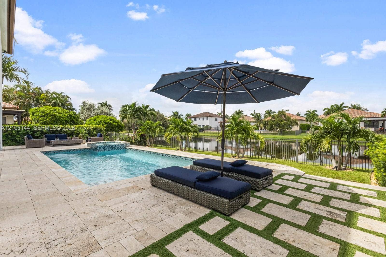 Outdoor area featuring a swimming pool with an integrated spillover spa, expansive stone paver deck, and decorative stone and grass hardscaping