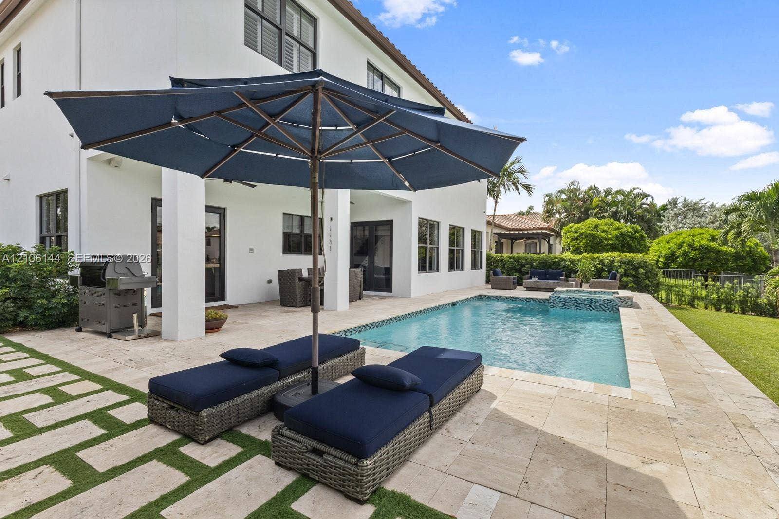 Outdoor area featuring a swimming pool with integrated spa, stone paver decking, grass-inlay hardscaping, and a covered patio