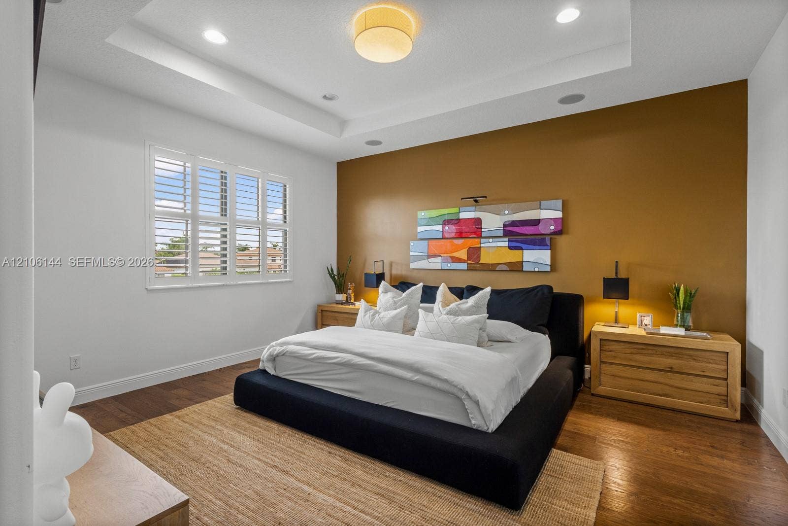 Tray ceiling with recessed lighting, wood-finish flooring, and window shutters