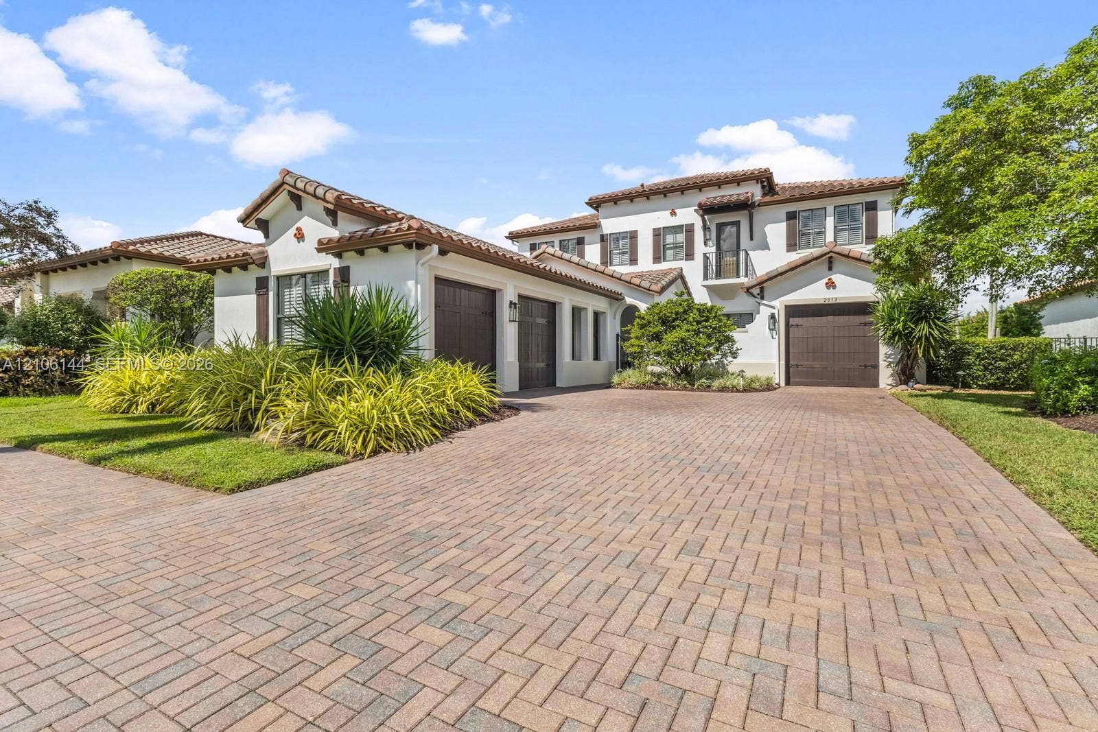 Mediterranean-style architecture featuring a tile roof, stucco exterior, paved herringbone driveway, three-car garage, and a second-story balcony