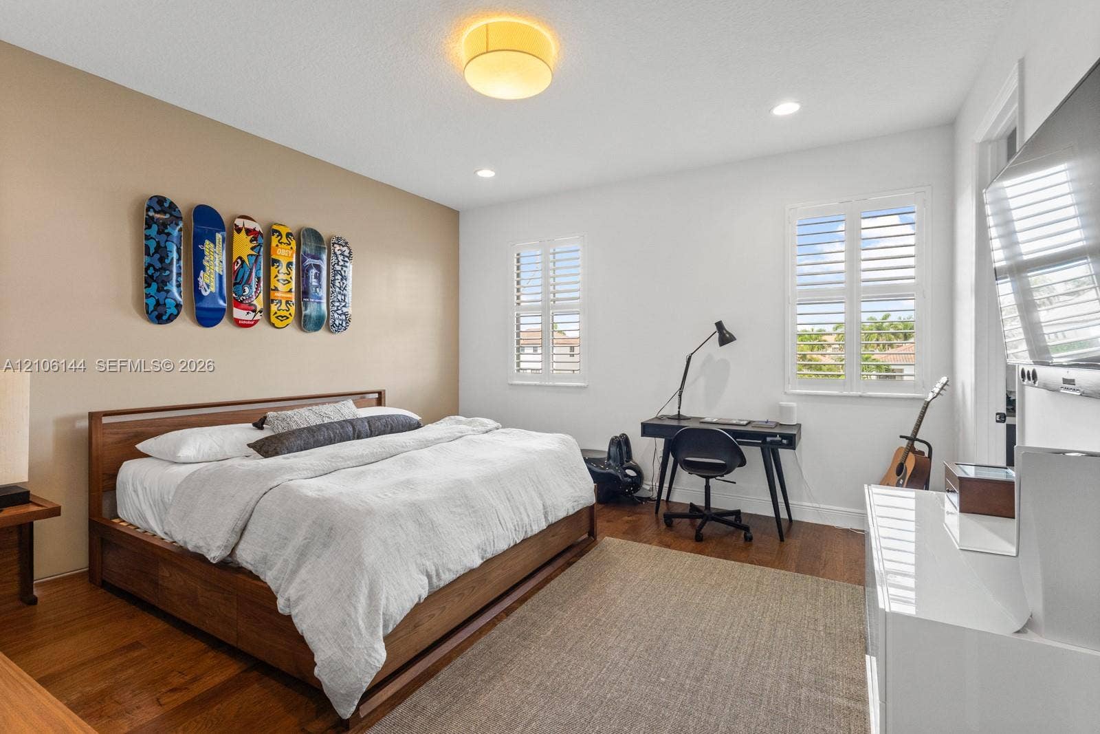 Room featuring wood-finish flooring, dual windows with plantation shutters, recessed lighting, and a neutral-toned accent wall