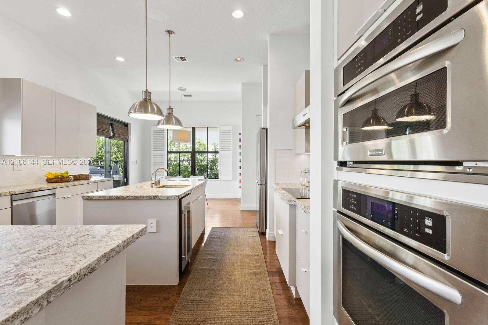 Kitchen featuring stone-finish countertops, stainless steel wall-mounted double ovens, flat-panel cabinetry, a center island with an integrated sink, and recessed lighting