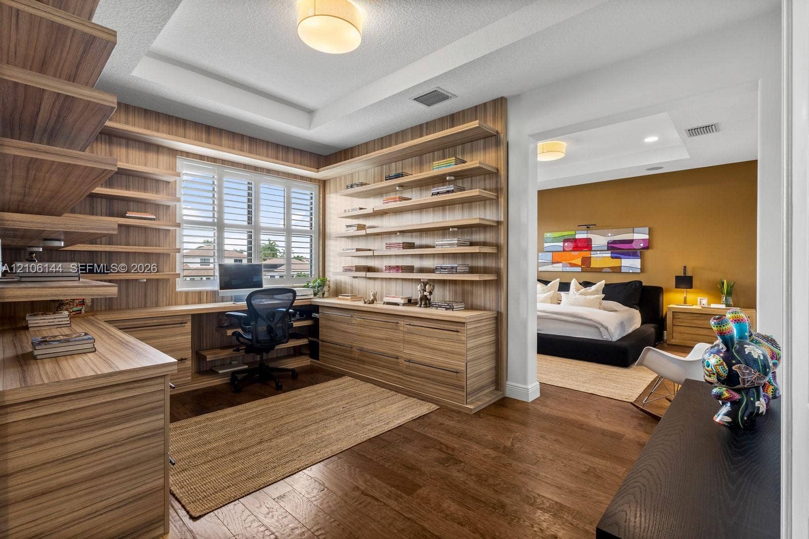 Custom wood-finish cabinetry featuring integrated open shelving and a built-in desk surface, complemented by tray ceilings, wood-finish flooring, and white plantation shutters