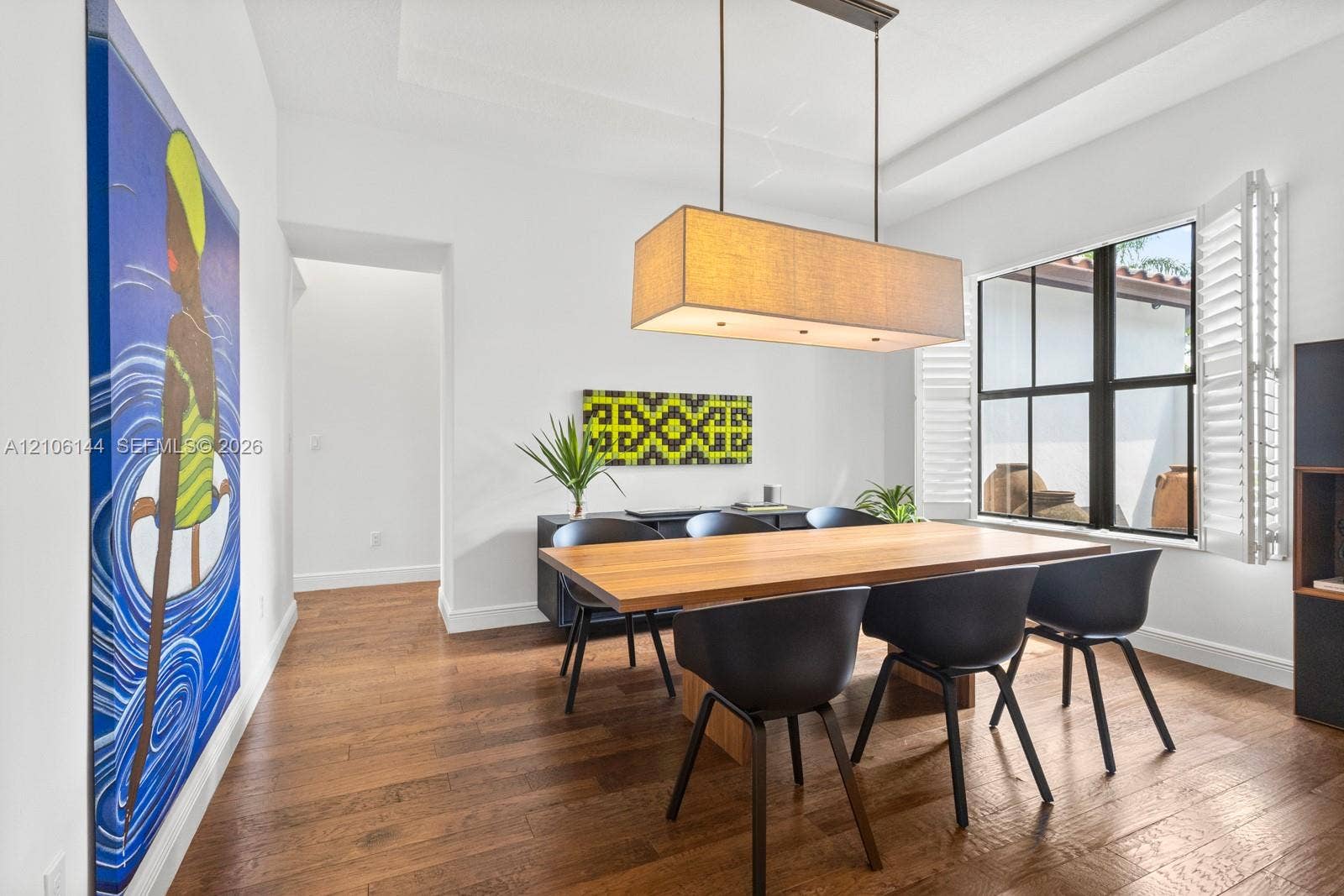 Interior space featuring wood-finish flooring, a tray ceiling, rectangular fabric-shade pendant lighting, and multi-pane windows with integrated shutters