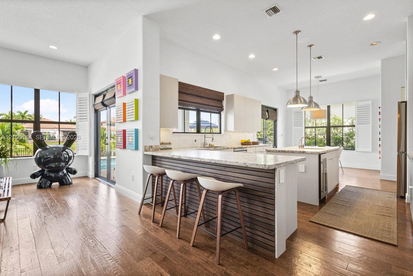 Kitchen featuring wood-finish flooring, a horizontal slat-paneled island, stone-surfaced countertops, recessed lighting, and metal pendant fixtures