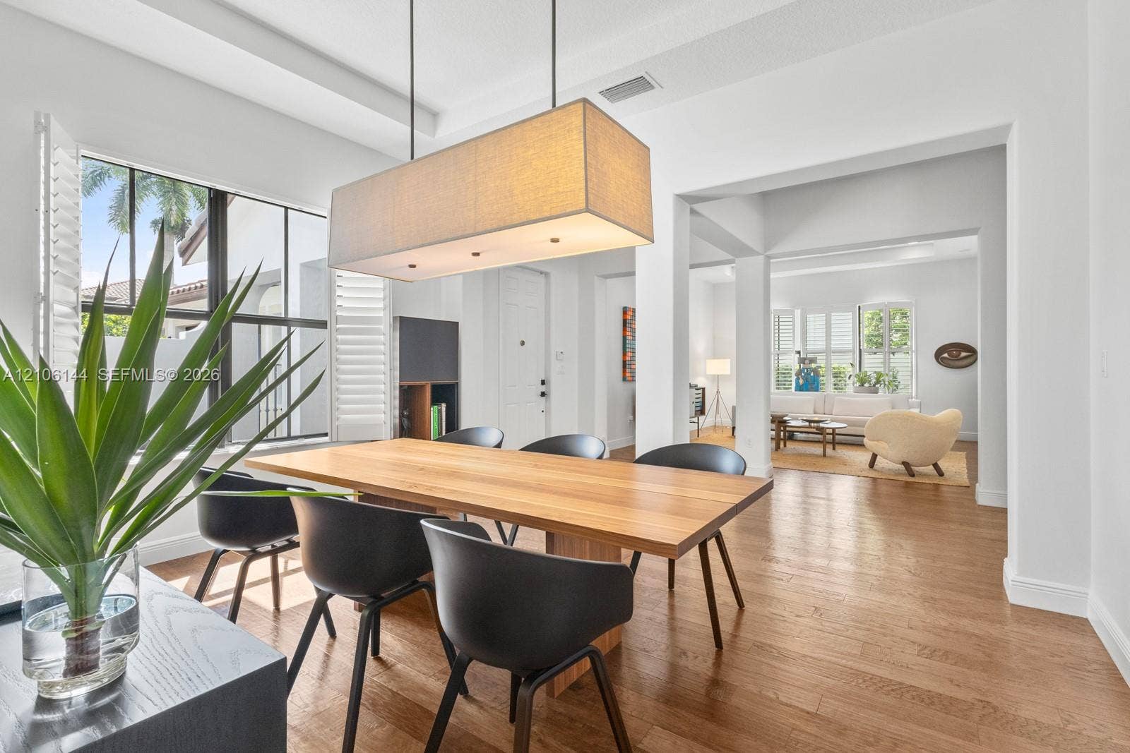 Open-concept dining area featuring wood-finish flooring, tray ceiling, rectangular fabric-shaded pendant lighting, and oversized multi-pane windows with plantation shutters