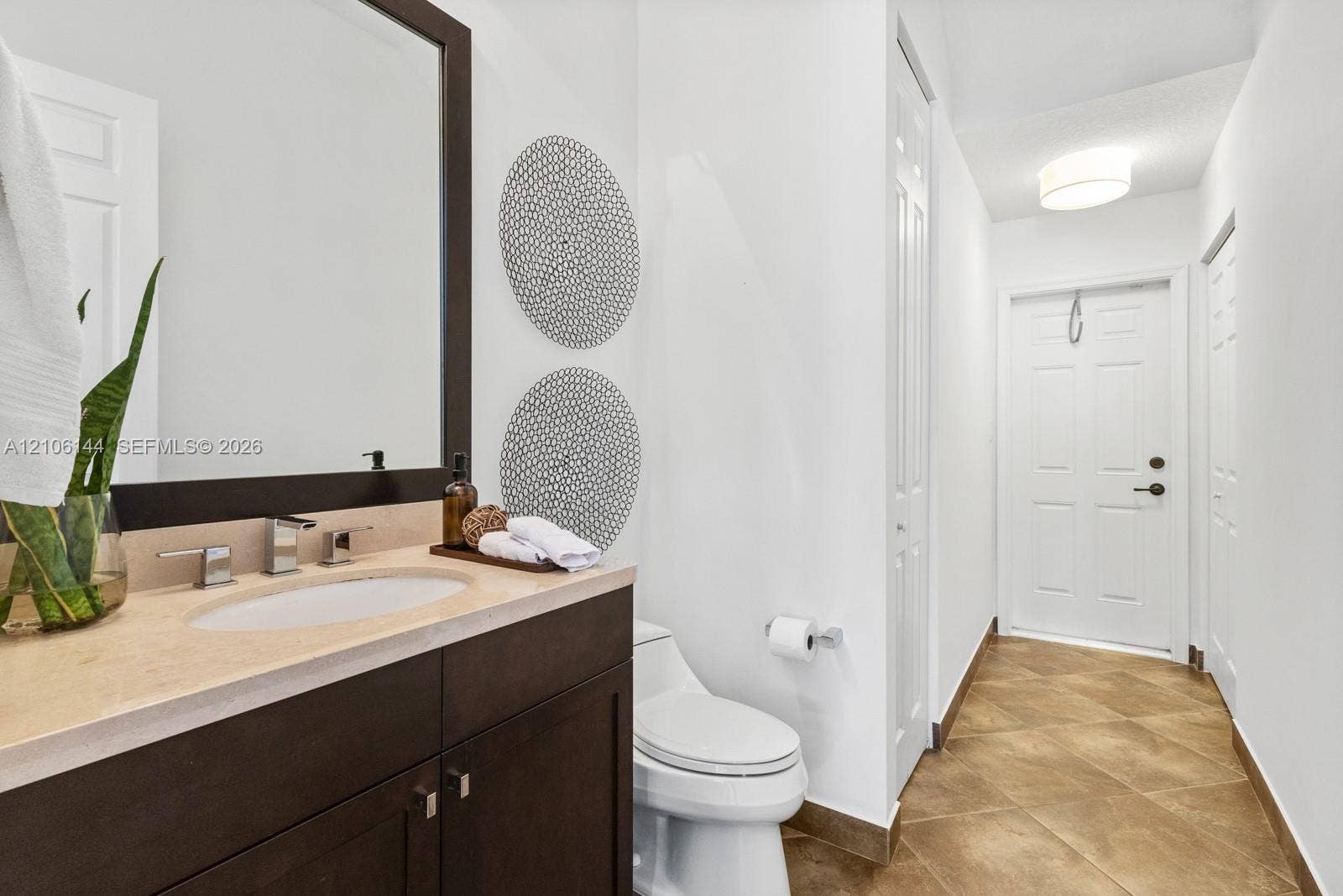 Dark wood vanity with a stone countertop, oval undermount sink, matching framed mirror, and tile flooring