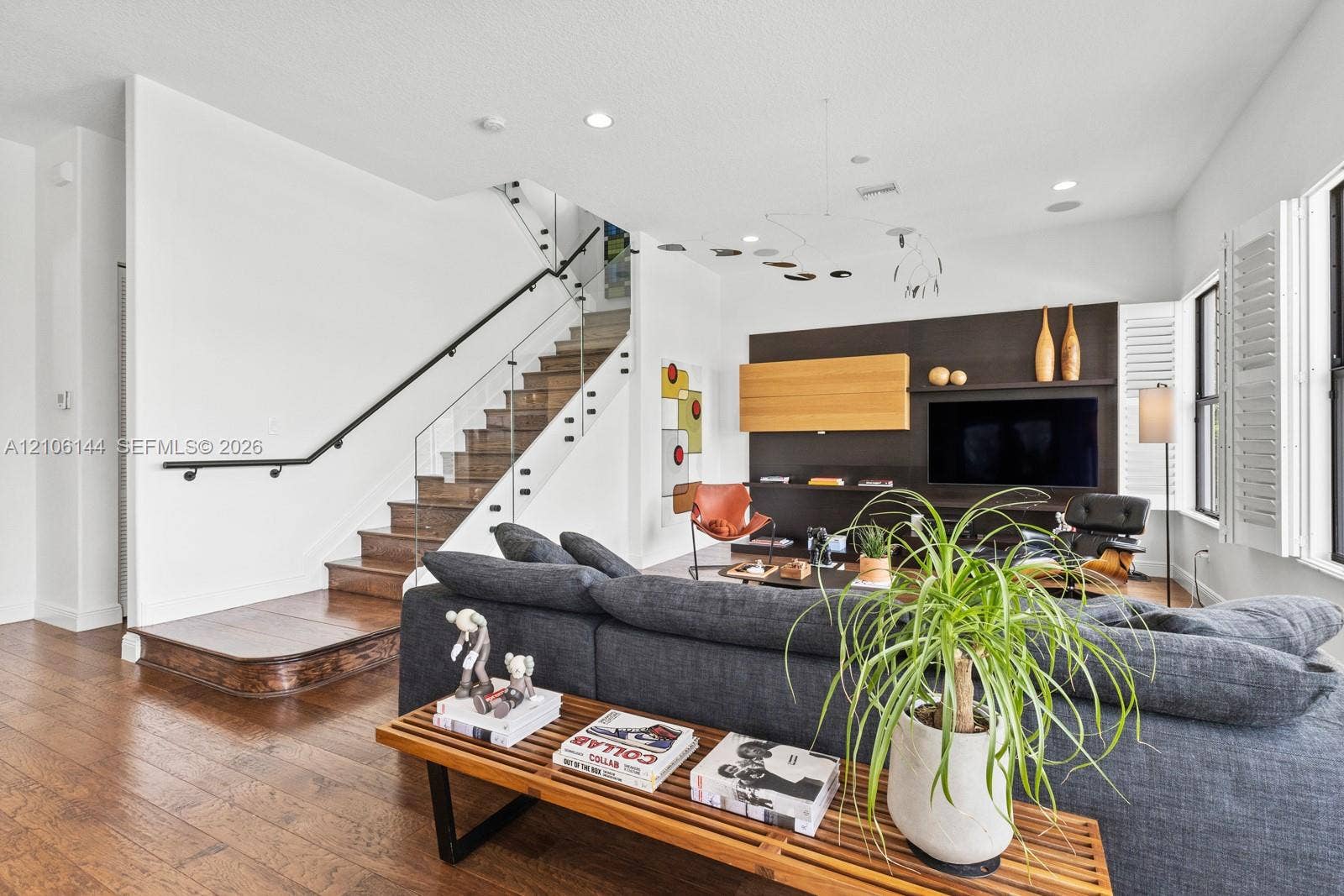 Staircase featuring wood-finish treads and a glass balustrade with a metal handrail, dark-toned custom built-in media cabinetry, recessed lighting, and wood-finish flooring
