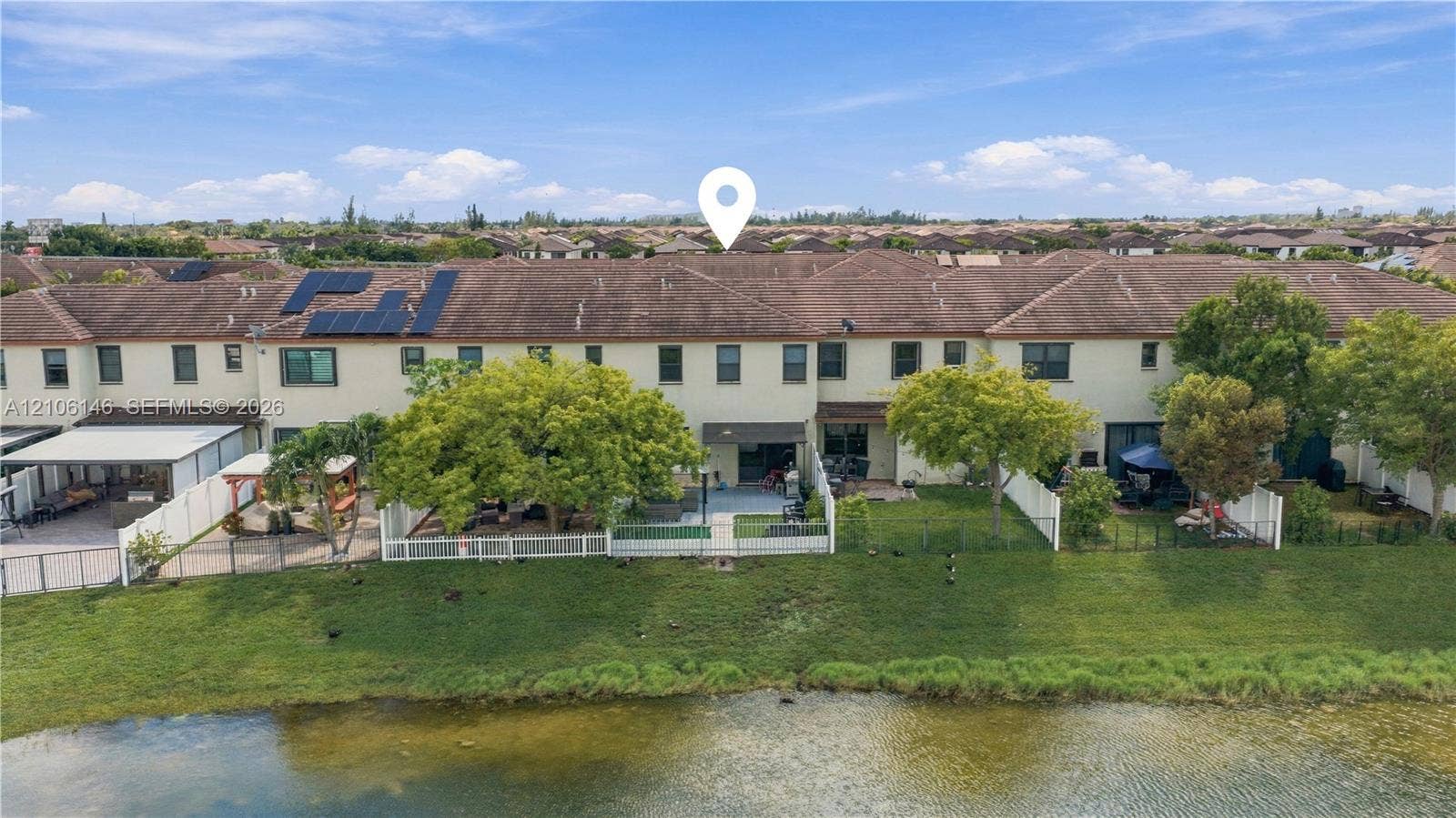 3259 W 100th Terrace, Hialeah, FL 33018 Two-story townhome exterior featuring stucco siding, a tiled roof, rooftop solar panels, private fenced rear yard, and direct water frontage