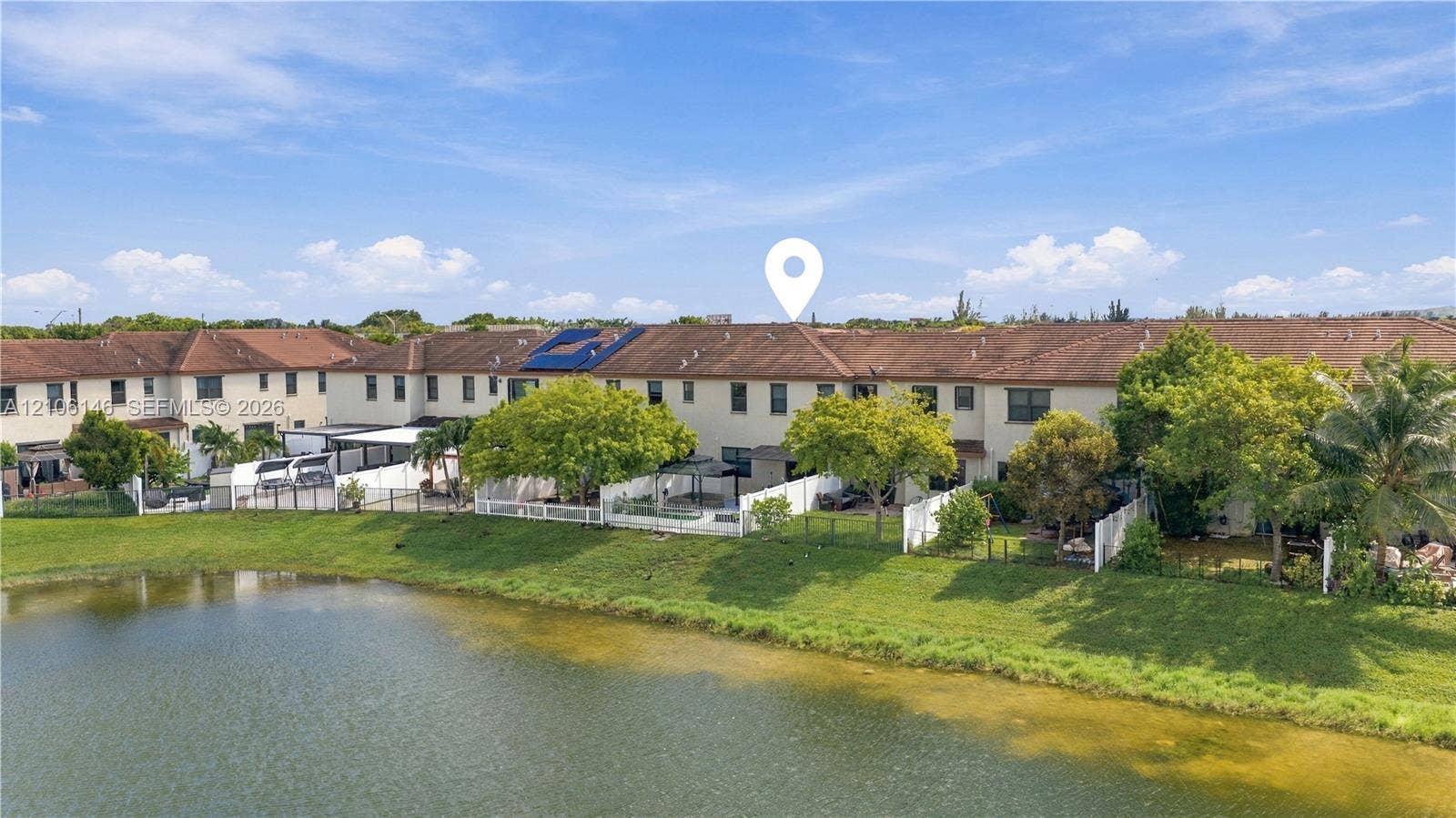 3259 W 100th Terrace, Hialeah, FL 33018 Stucco exterior townhouse featuring a tile roof, solar panels, and a private enclosed rear patio situated on a pond