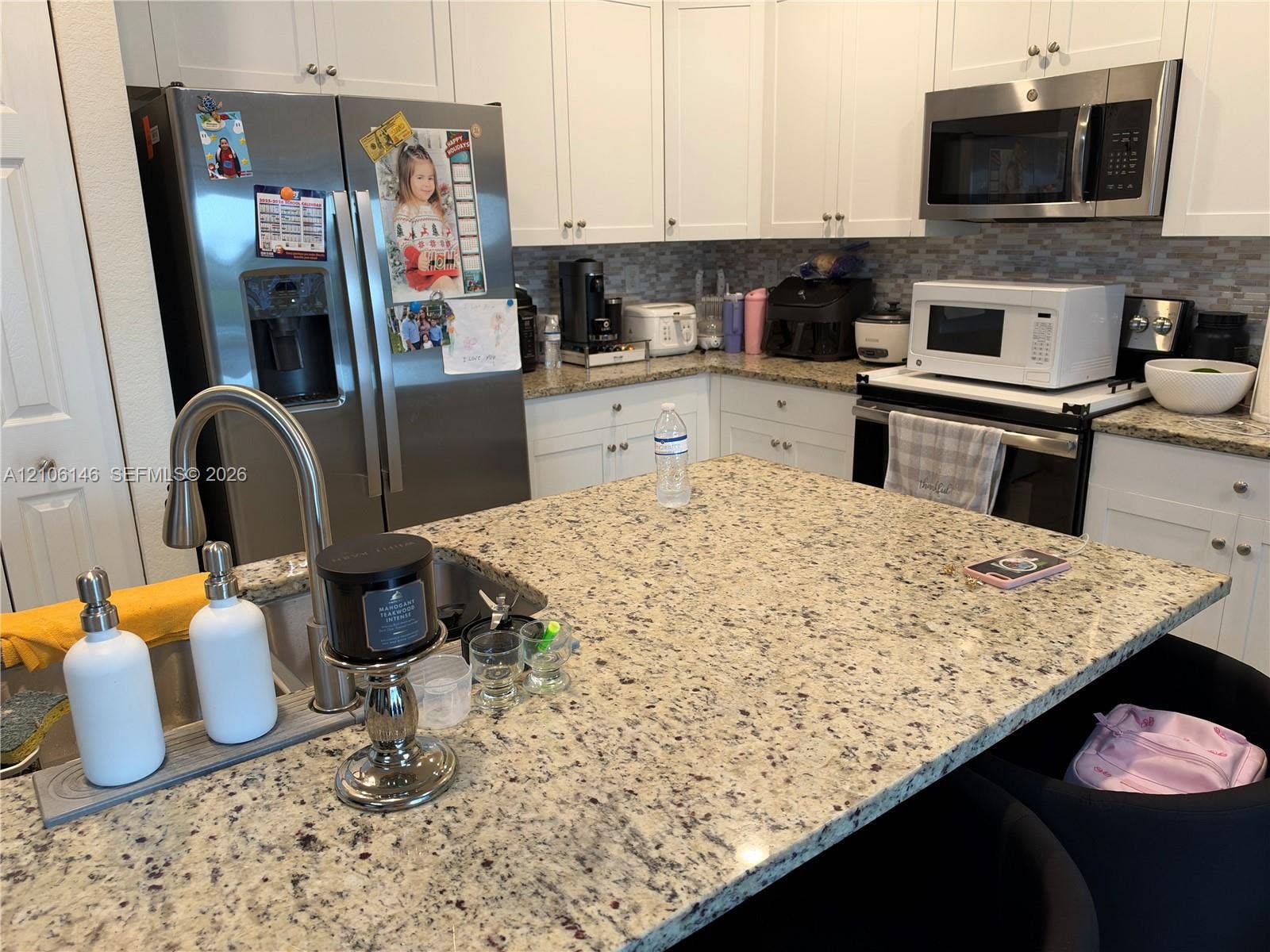 3259 W 100th Terrace, Hialeah, FL 33018 Kitchen featuring a central island with stone countertop, stainless steel appliances, white cabinetry, and a mosaic tile backsplash