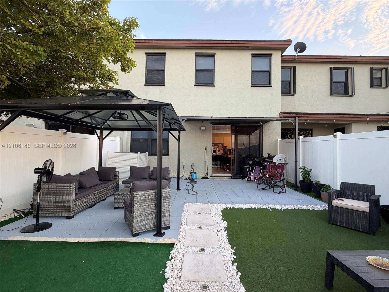 3259 W 100th Terrace, Hialeah, FL 33018 Backyard featuring a paved patio, synthetic turf lawn, white vinyl perimeter fencing, and stone-bordered walkway