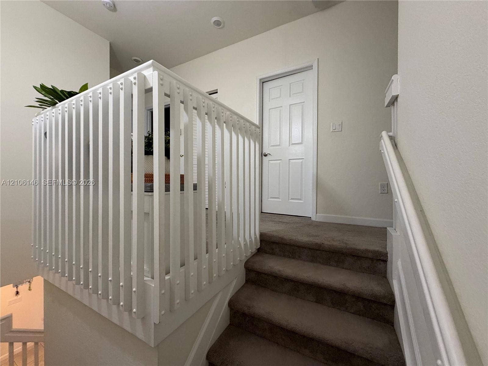 3259 W 100th Terrace, Hialeah, FL 33018 White vertical-slat stair railing with a matching handrail and carpeted staircase featuring a six-panel door
