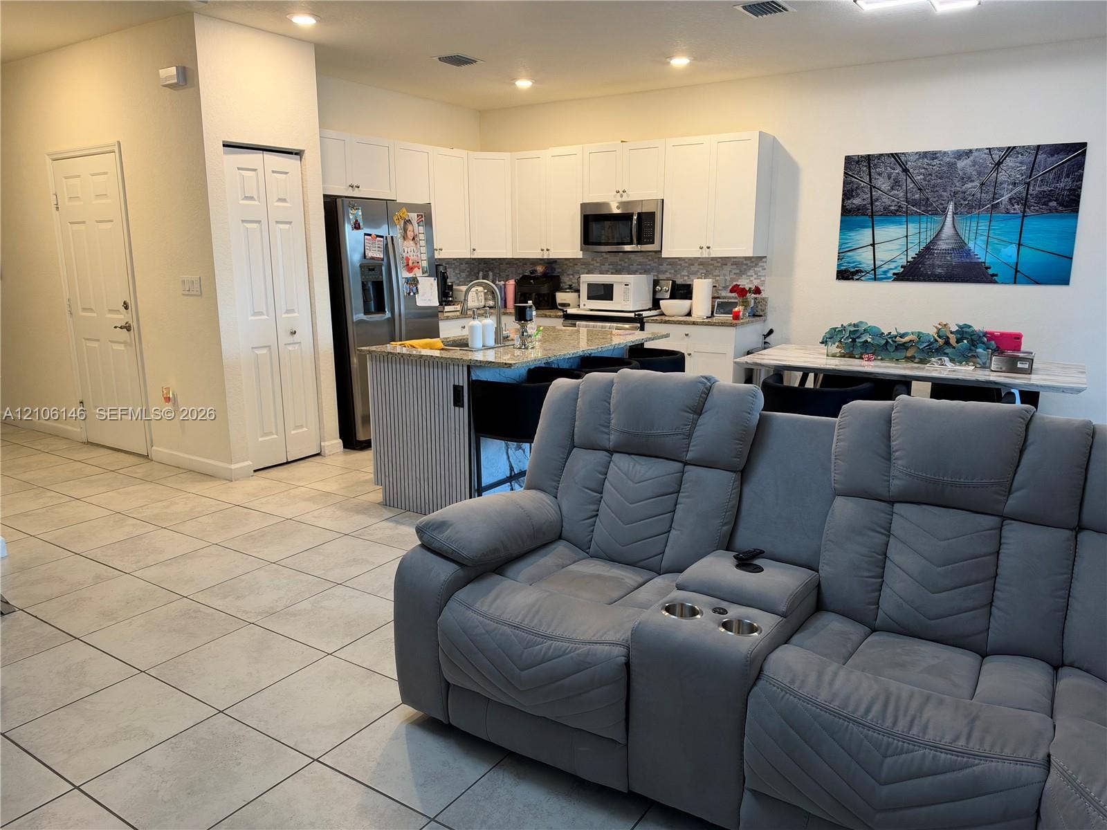 3259 W 100th Terrace, Hialeah, FL 33018 Kitchen featuring white shaker-style cabinetry, stone-finish countertops, a central island with a fluted detail finish, stainless steel appliances, and large-format ceramic tile flooring