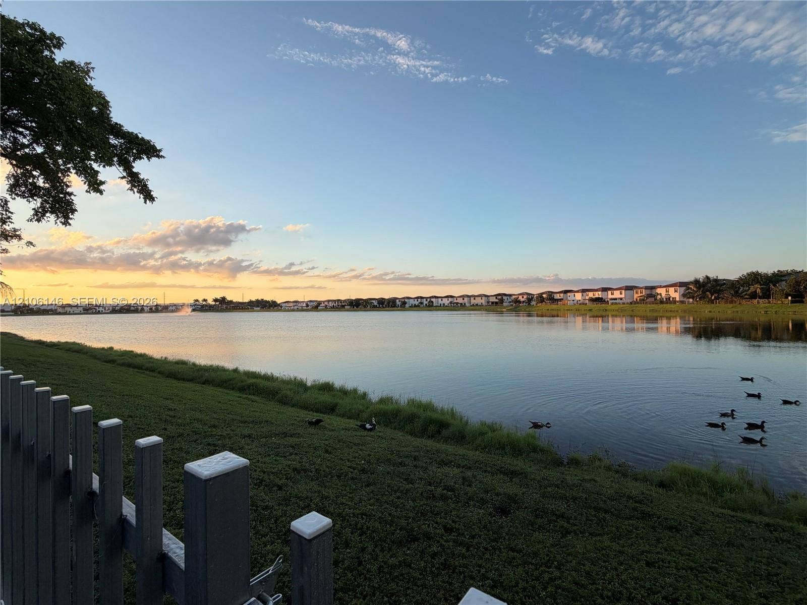 3259 W 100th Terrace, Hialeah, FL 33018 Waterfront property featuring a lake, sloped grass embankment, and vinyl post-and-rail fencing