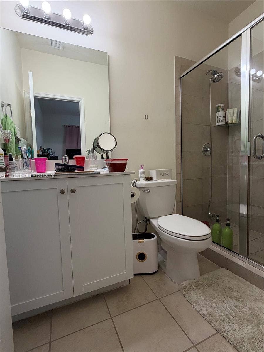 3259 W 100th Terrace, Hialeah, FL 33018 White vanity cabinet with a countertop, large vanity mirror, four-light vanity fixture, and a tiled shower enclosure with a glass door