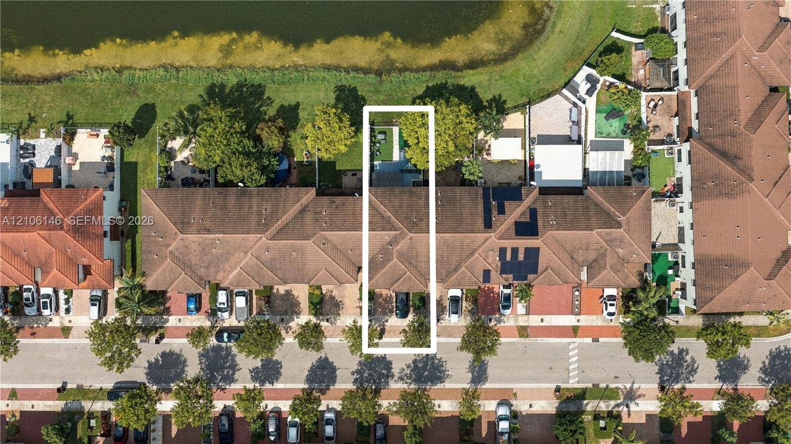 3259 W 100th Terrace, Hialeah, FL 33018 Aerial perspective of a multi-unit property featuring a shingled roof, paved driveway, dedicated parking space, and rear yard area bordering a water feature