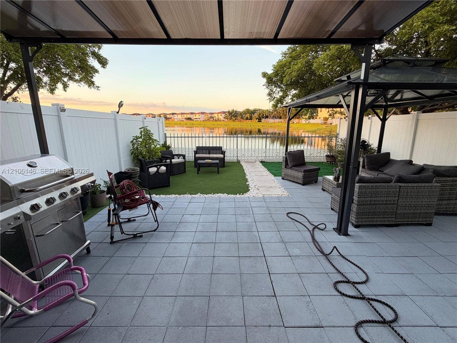 3259 W 100th Terrace, Hialeah, FL 33018 Paved patio featuring a metal gazebo, synthetic turf lawn, white vinyl fencing, and lake frontage