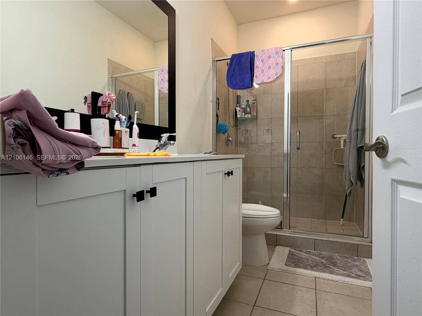 3259 W 100th Terrace, Hialeah, FL 33018 Bathroom featuring a white shaker-style vanity with matte black hardware, a large framed mirror, tiled flooring, and a walk-in shower with a glass enclosure and tiled surround