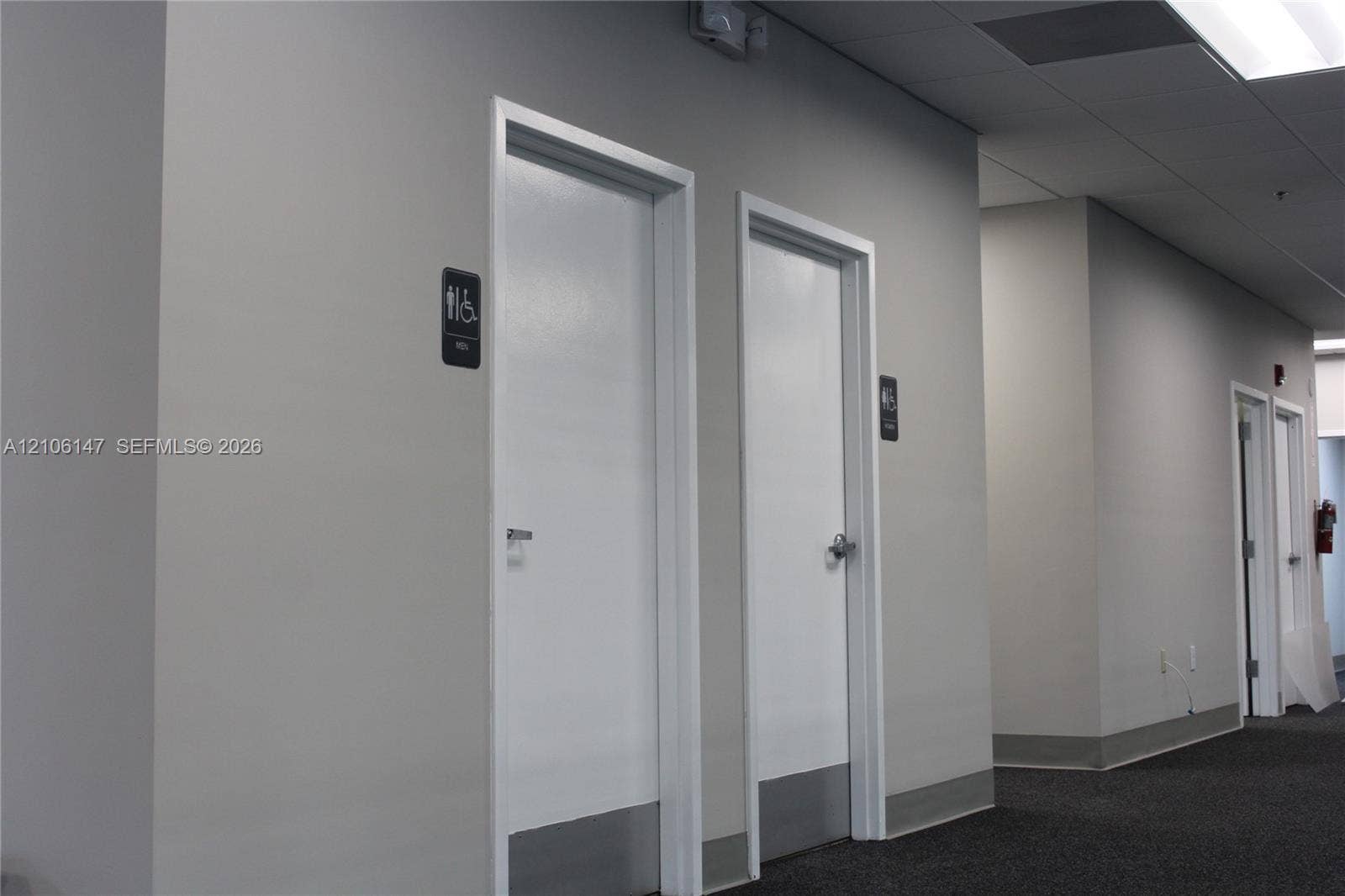 Commercial hallway featuring neutral-toned walls, recessed ceiling lighting, carpeting, and multiple interior doors with metal kick plates