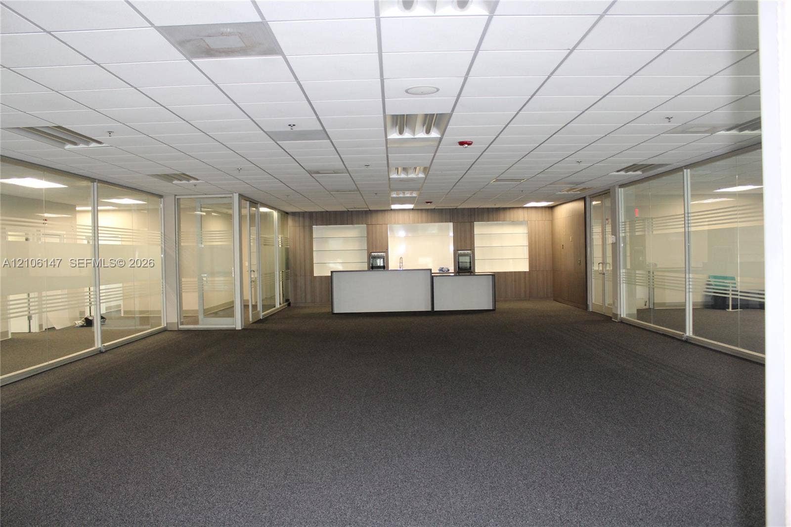 Open floor plan office space featuring integrated glass partitions, recessed lighting, carpeted flooring, and a built-in service counter