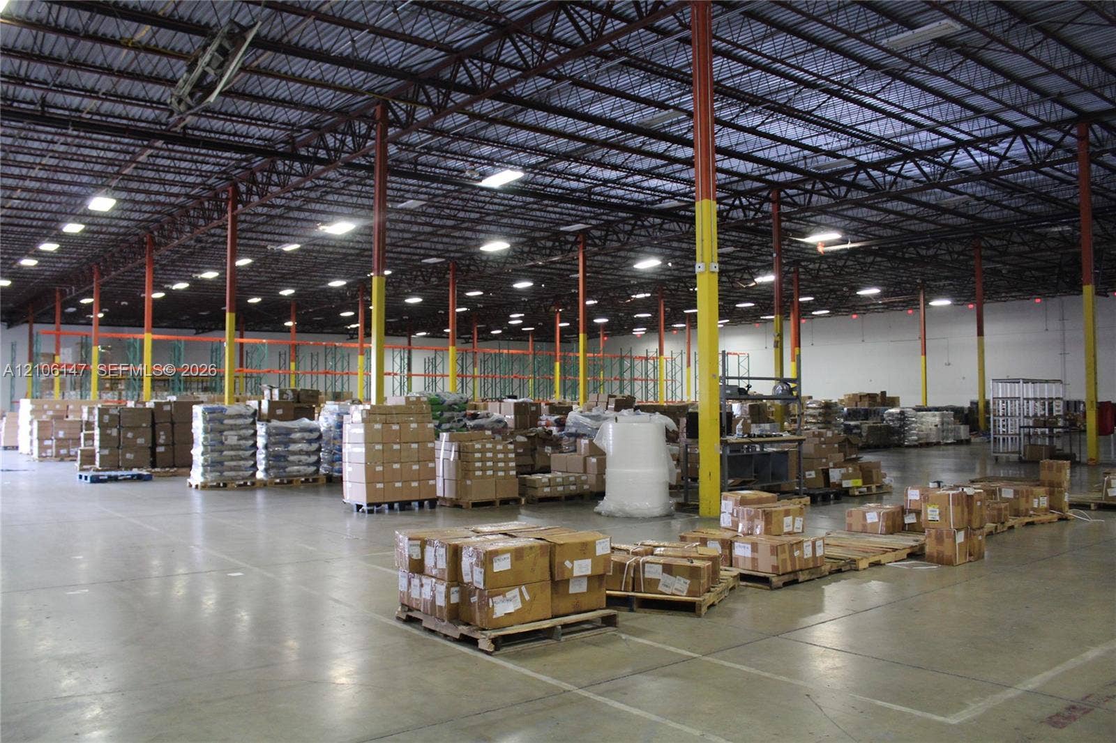 Industrial warehouse facility featuring high-clearance exposed steel truss ceilings, polished concrete flooring, extensive overhead LED lighting, and structural support columns