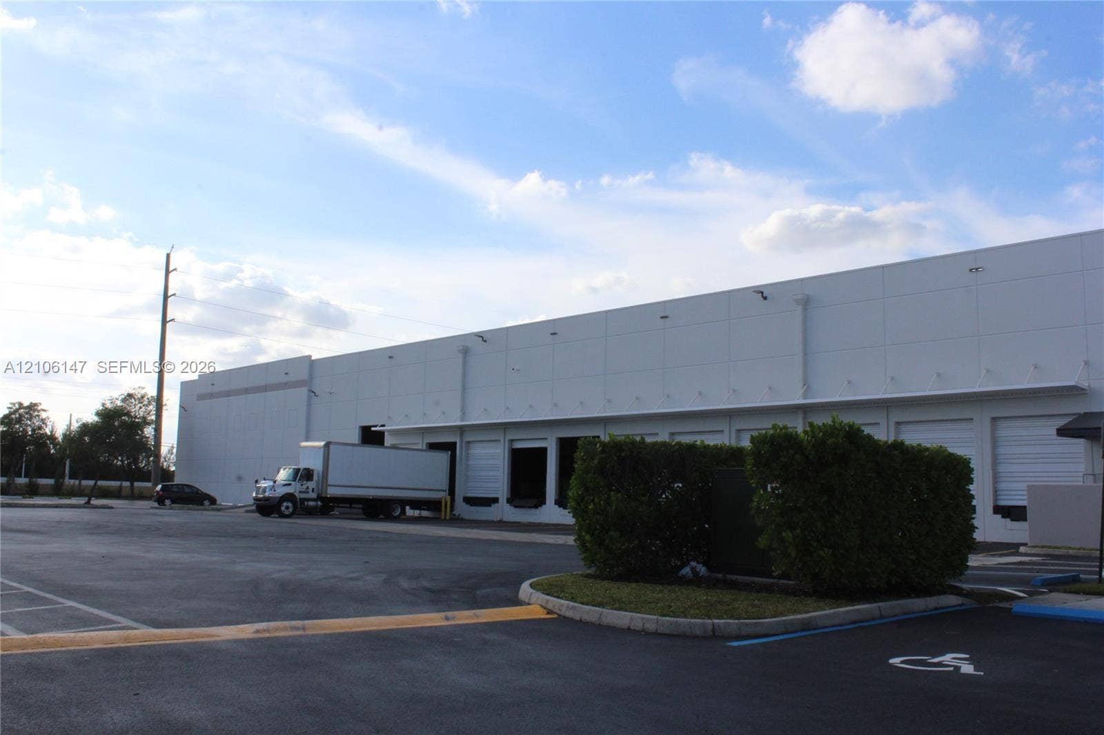 Industrial facility exterior featuring multiple loading docks, an expansive asphalt-paved lot, and white precast concrete panels