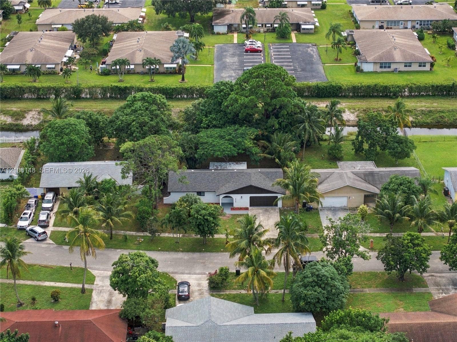 2920 Dorson Way, Delray Beach, FL 33445 Aerial perspective of a single-story residence featuring a shingled roof, a paved driveway, and mature landscaping with palm and shade trees