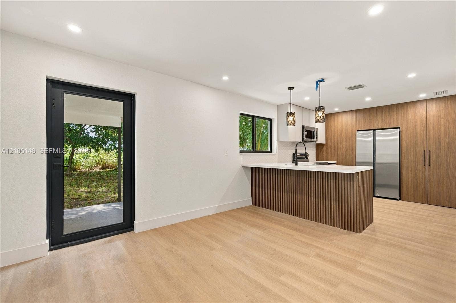 2920 Dorson Way, Delray Beach, FL 33445 Kitchen featuring wood-finish cabinetry, a slatted island base, recessed lighting, integrated stainless steel appliances, and a glass-paneled exterior door