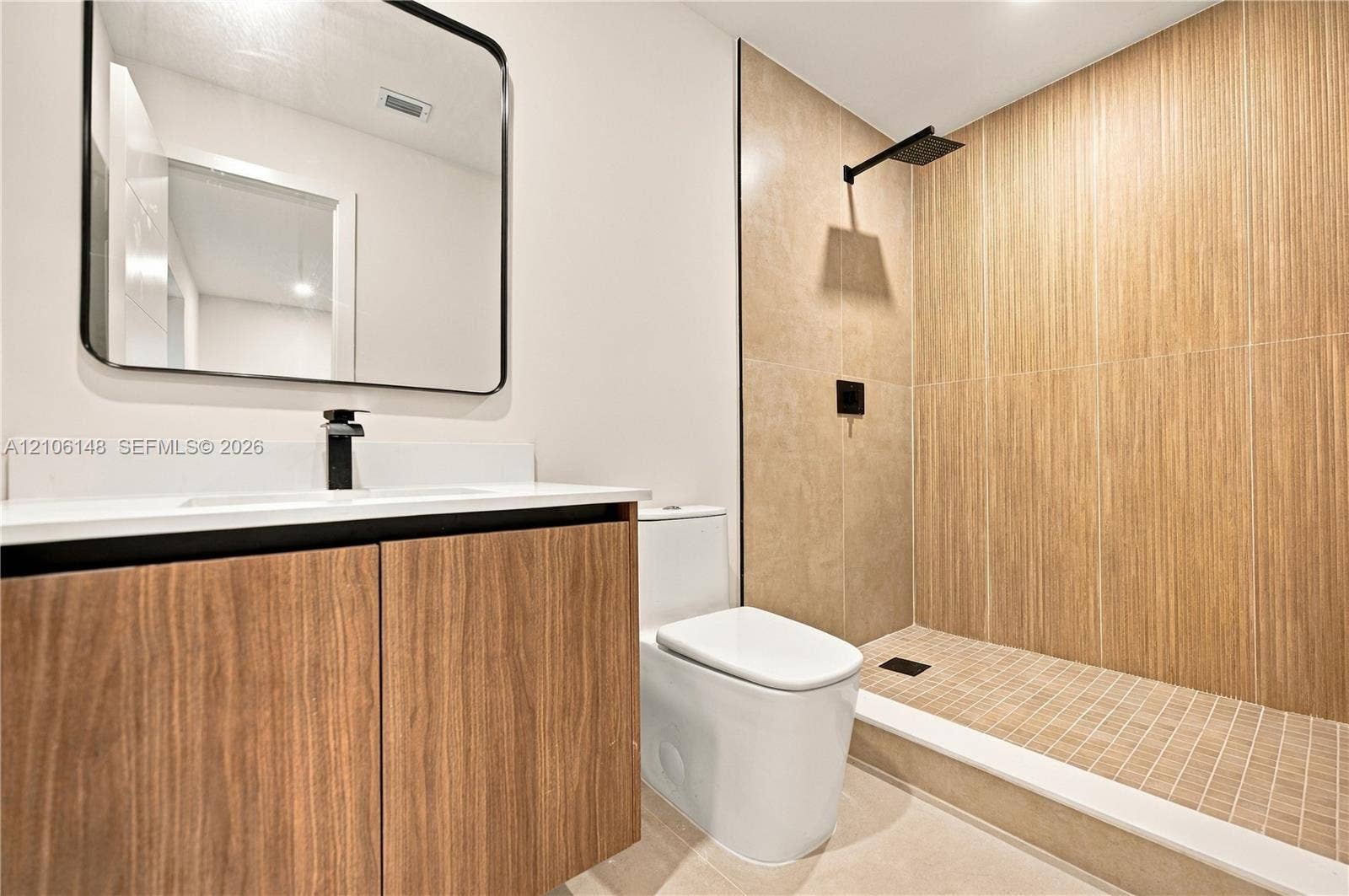 2920 Dorson Way, Delray Beach, FL 33445 Bathroom featuring a wood-finish floating vanity, wall-mounted matte black faucet, rectangular mirror with a black frame, and a walk-in shower with vertical wood-texture tile and rain showerhead