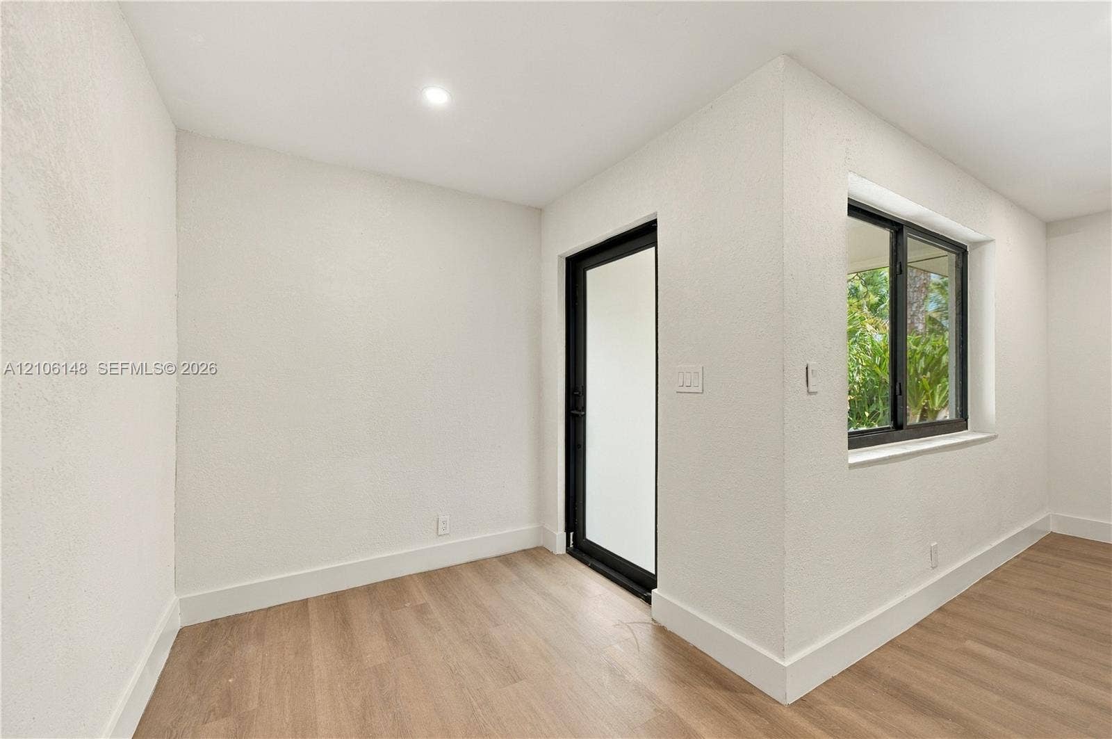 2920 Dorson Way, Delray Beach, FL 33445 Interior space featuring wood-finish flooring, textured white walls, a black-framed glass exterior door, and a black-framed window