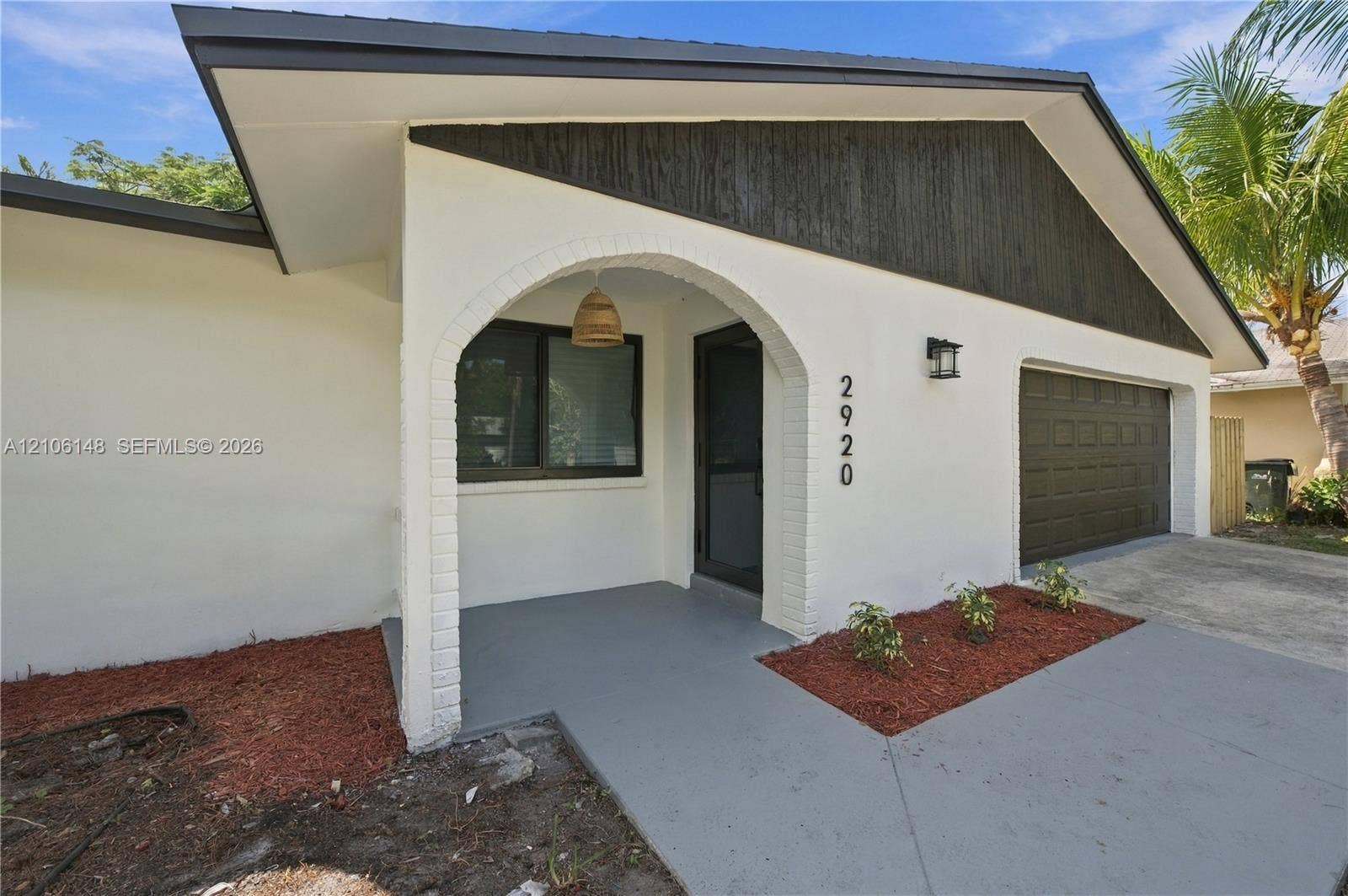 2920 Dorson Way, Delray Beach, FL 33445 Single-story residence featuring a stucco exterior, arched covered entryway, dark wood-finish gable accent, and a single-car garage