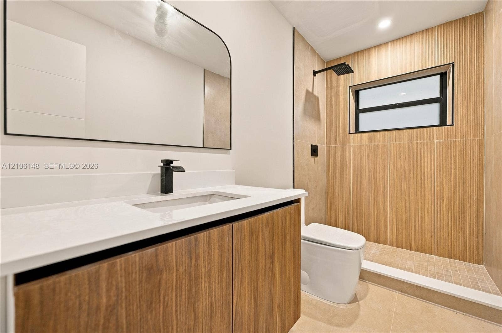 2920 Dorson Way, Delray Beach, FL 33445 Floating vanity with wood-finish cabinetry, white countertop, arched mirror, matte black fixtures, and walk-in shower with vertical-tiled surround