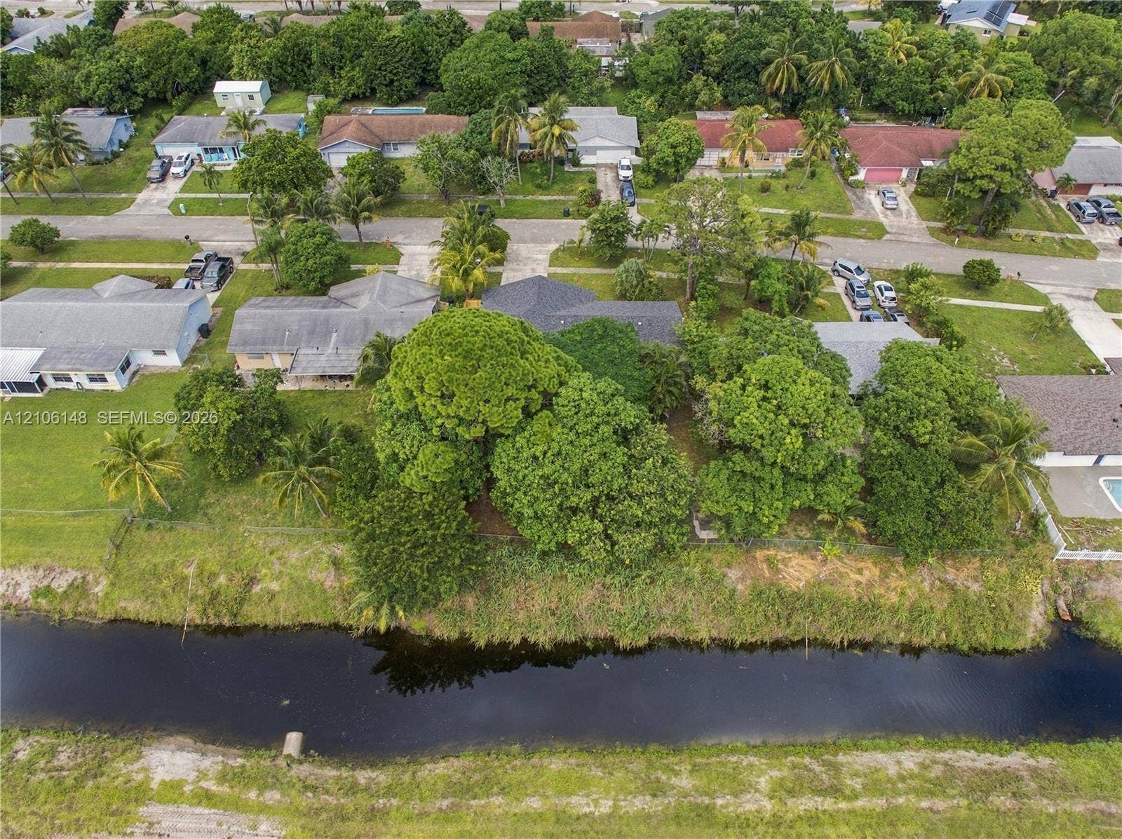 2920 Dorson Way, Delray Beach, FL 33445 Aerial perspective featuring a waterfront lot, mature trees, and a residential structure with an asphalt shingle roof