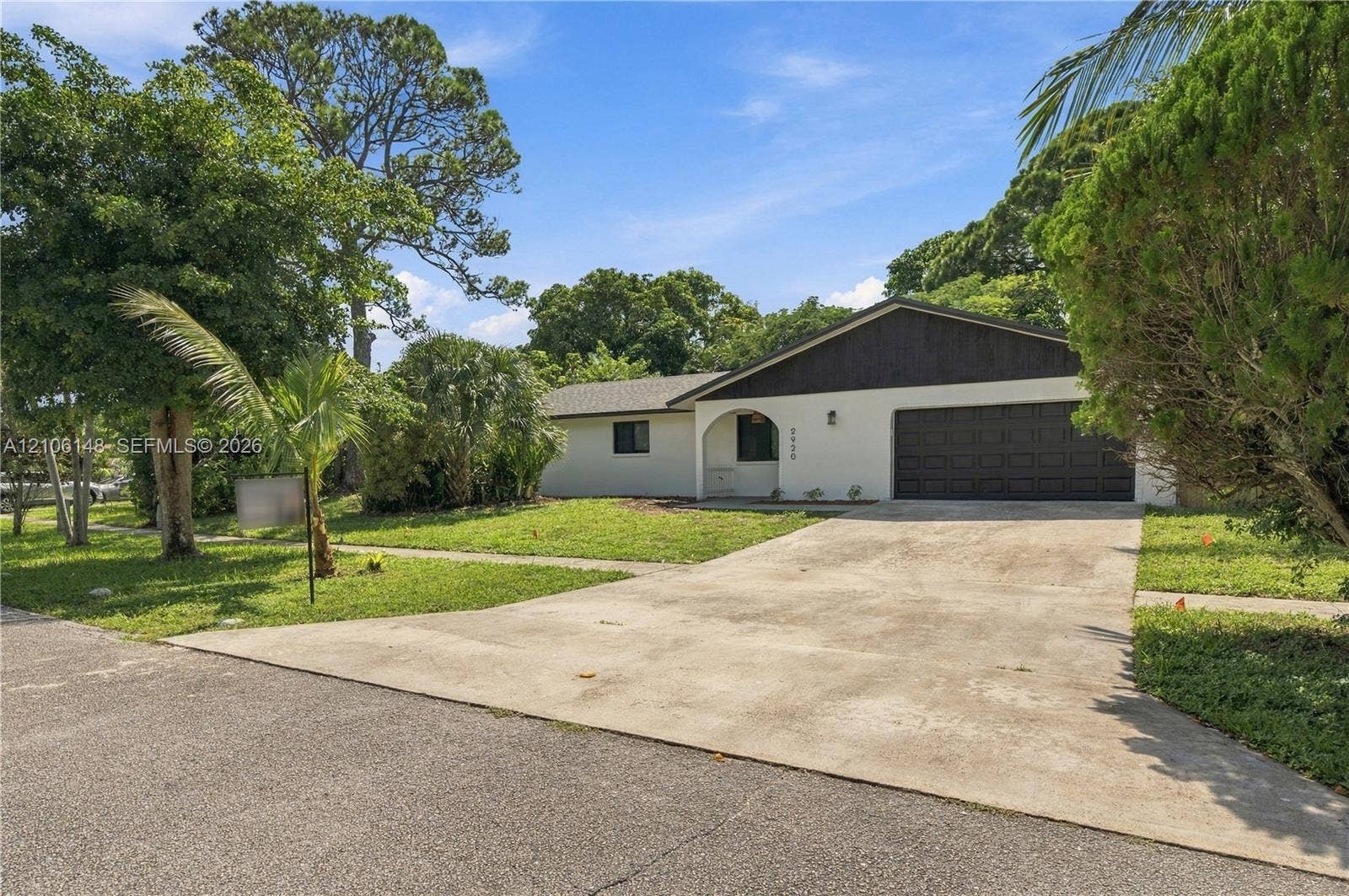 2920 Dorson Way, Delray Beach, FL 33445 Single-story exterior featuring a light-colored stucco facade, contrasting dark wood-finish siding, a concrete driveway, and an arched entryway