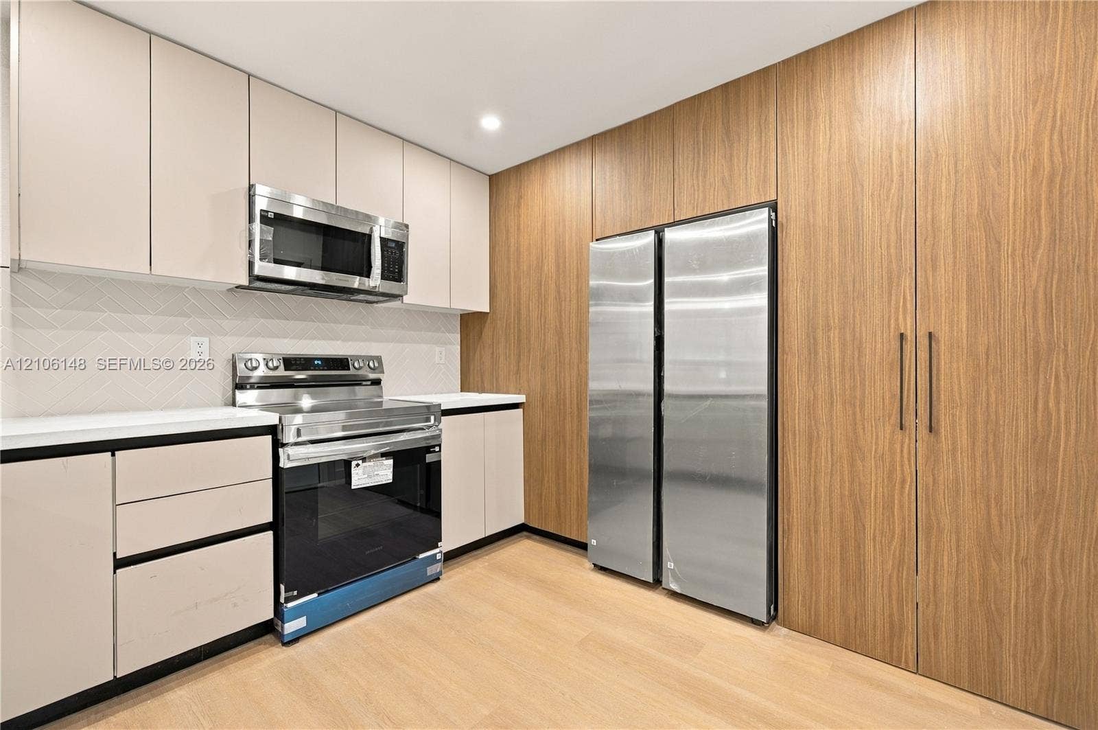 2920 Dorson Way, Delray Beach, FL 33445 Kitchen featuring sleek flat-panel cabinetry, floor-to-ceiling wood-finish storage, stainless steel appliances, light-toned countertop, and chevron-patterned backsplash