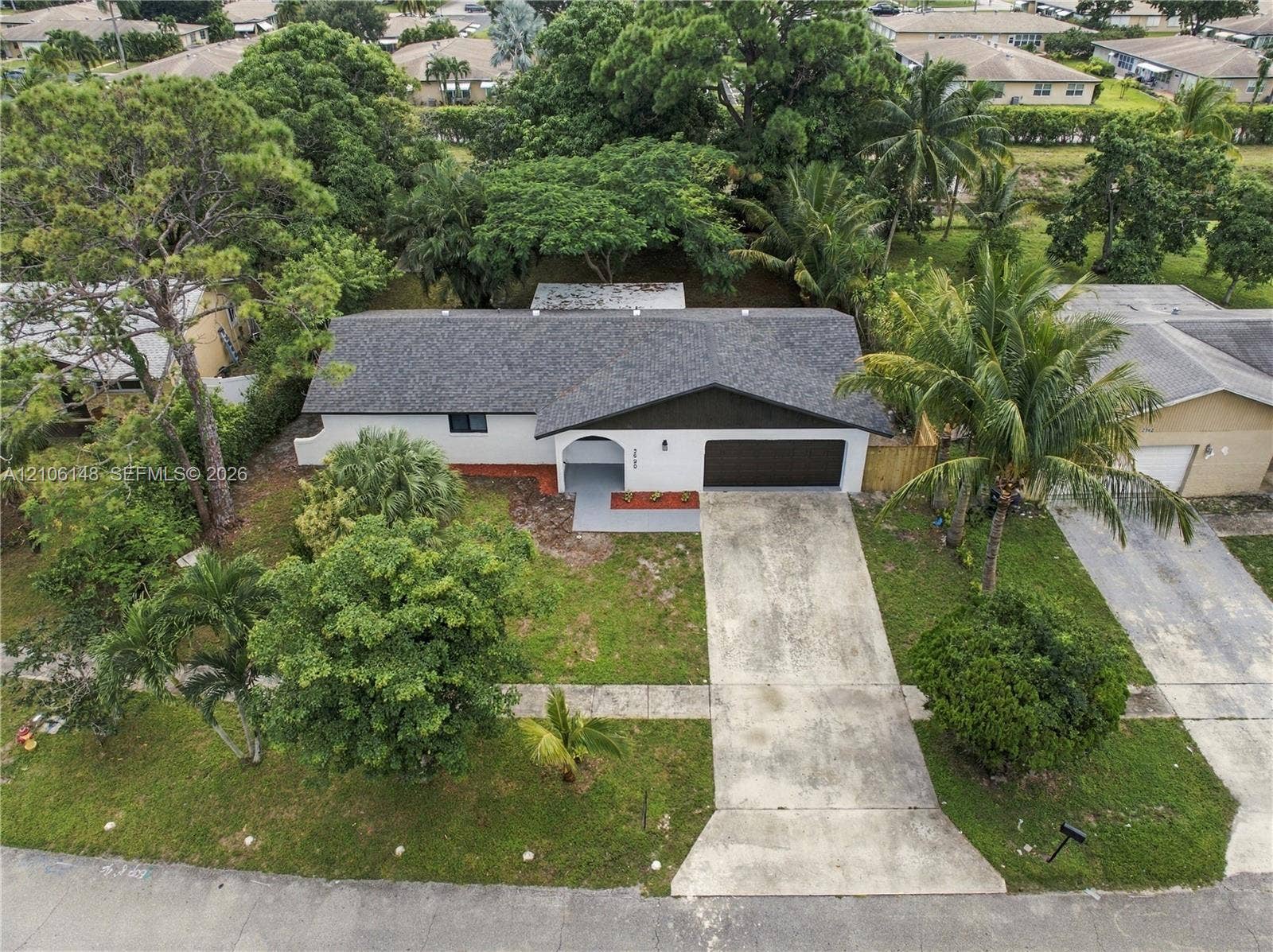 2920 Dorson Way, Delray Beach, FL 33445 Single-story residence featuring an asphalt shingle roof, a two-car garage, an arched entryway, and a concrete driveway surrounded by mature landscaping