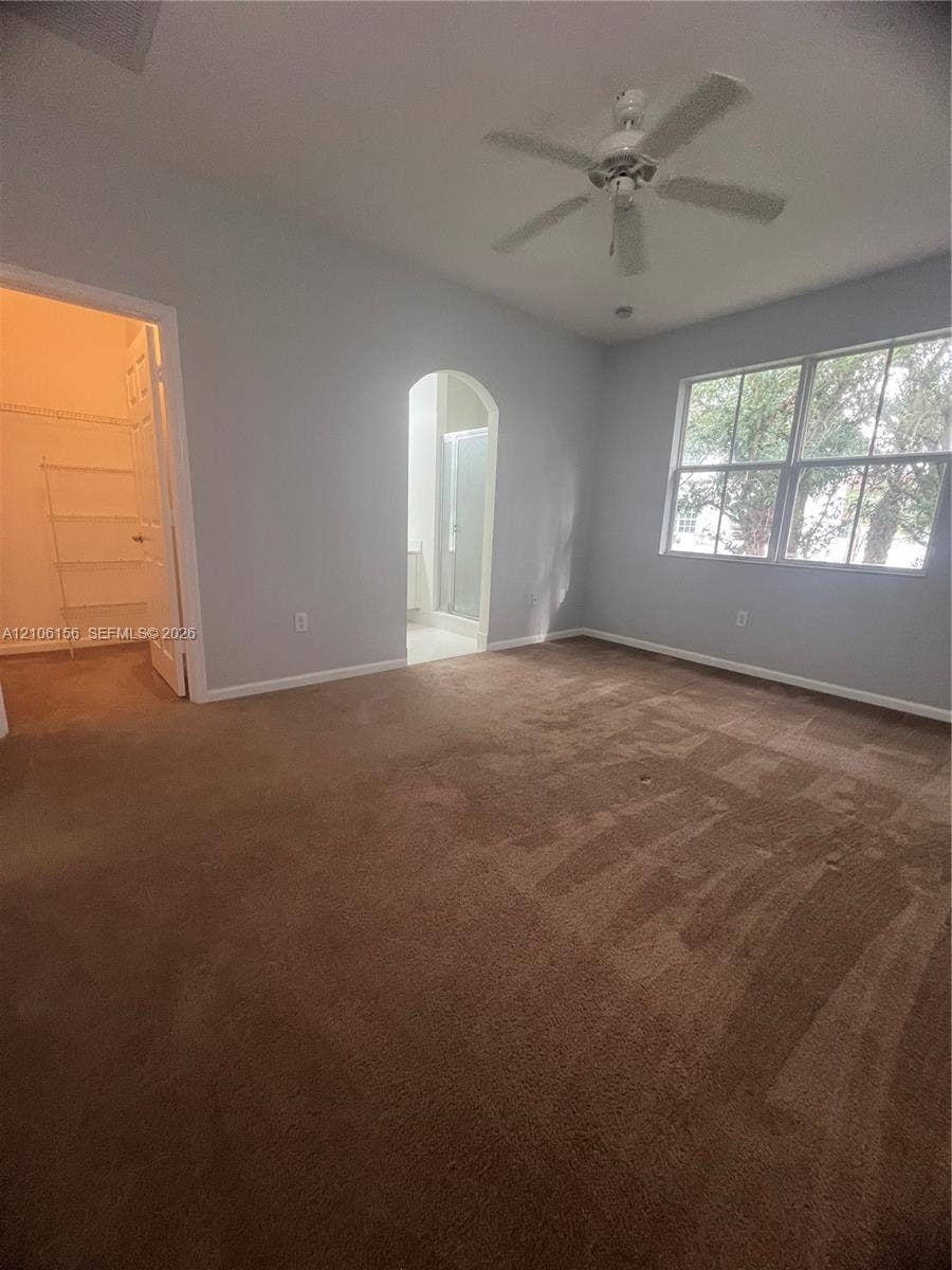 Room featuring neutral wall tones, carpeting, a ceiling fan, a multi-pane window, and an arched entry