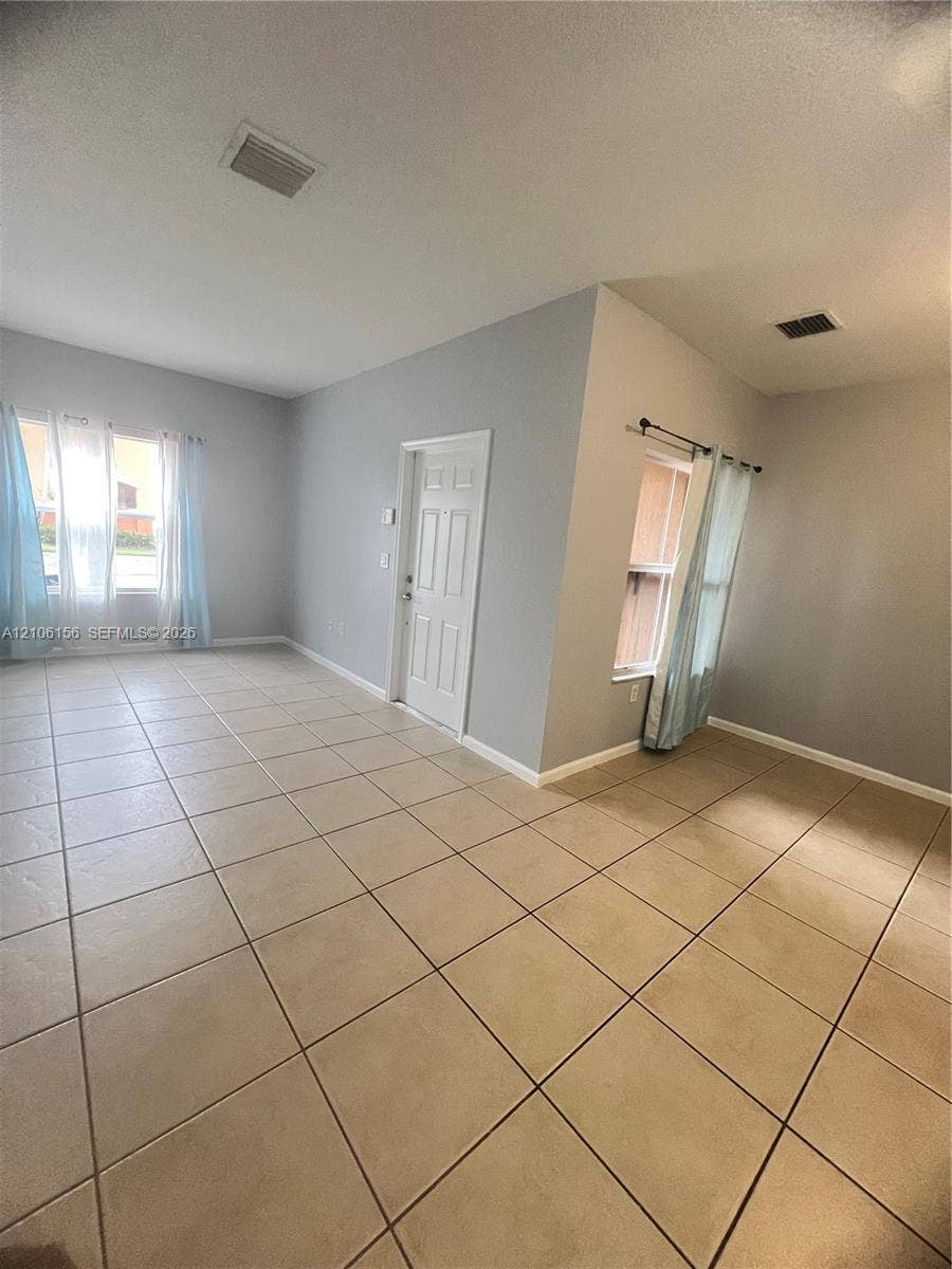 Neutral-toned interior space featuring light-colored ceramic tile flooring, neutral wall paint, and multiple windows providing natural illumination