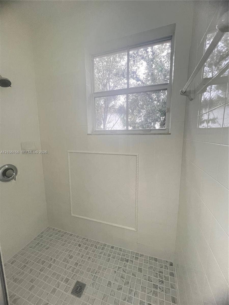 Walk-in shower featuring large-format wall tile, mosaic tile flooring, a window, a built-in recessed shelf, and chrome plumbing fixtures